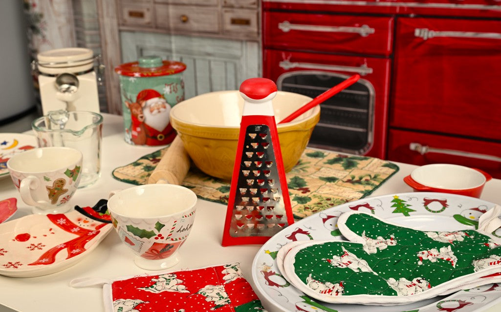 Christmas-themed kitchenware including plates, bowls, and a grater on a countertop with a red oven in the background.